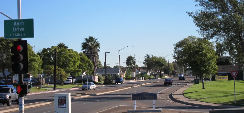 Tree-lined entrance to Serra Mesa from Aero Drive with the community sign in the median
